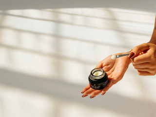 Person applying cream from a jar with a spoon on a light background
